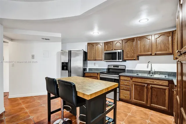 a kitchen with stainless steel appliances granite countertop a stove top oven a sink dishwasher a refrigerator and a dining table with wooden cabinet