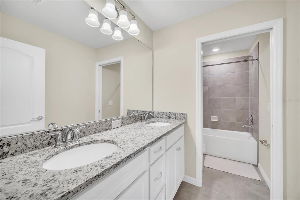 7196 Oakmoss Loop Davenport, FL 33837 - Photo 27 of 48 a bathroom with a granite countertop sink a mirror and a bathtub