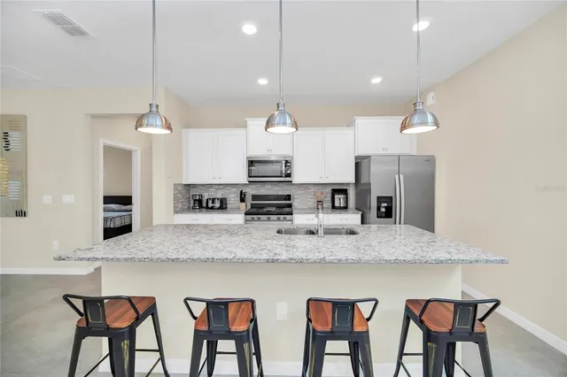 a large kitchen with granite countertop a counter space chairs stainless steel appliances and cabinets