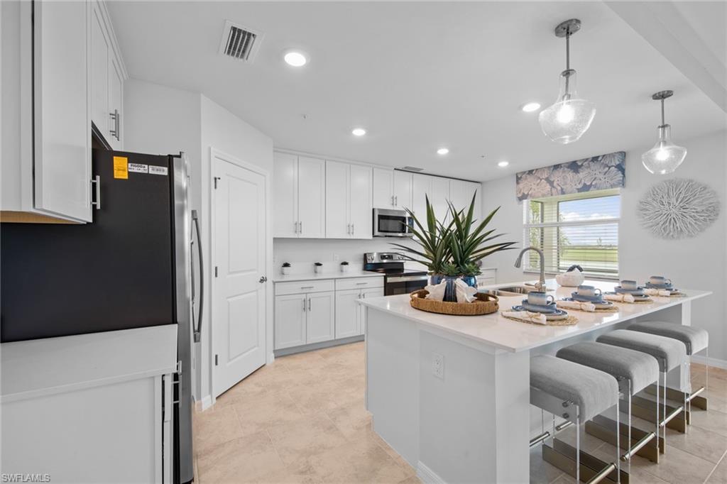 6008 Ellerston Way Avenue, Unit 1011 Immokalee, FL 34142 - Photo 15 of 50 Kitchen featuring stainless steel appliances, a kitchen bar, hanging light fixtures, white cabinets, and a center island with sink