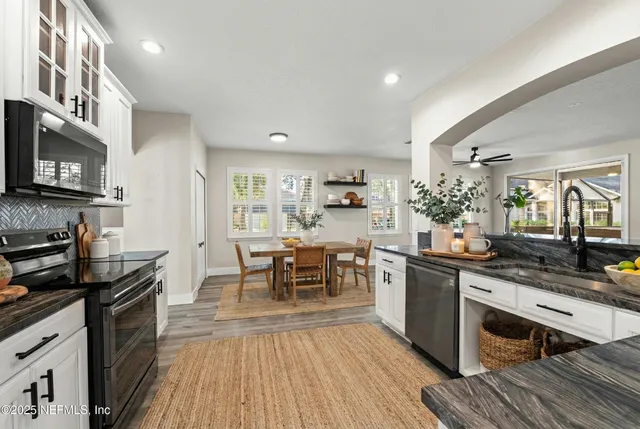 a large kitchen with stainless steel appliances granite countertop a stove top oven a sink dishwasher and a refrigerator with wooden floor