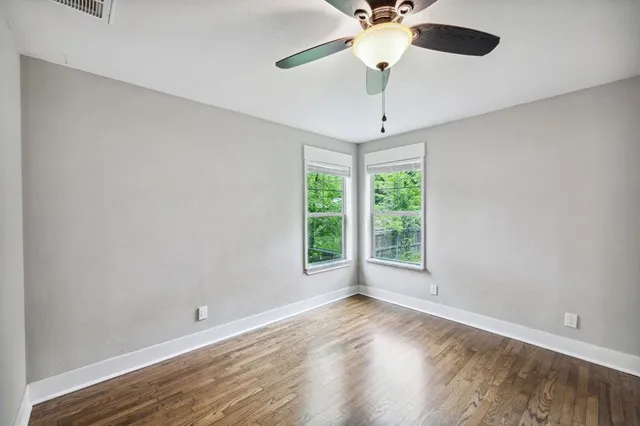 an empty room with wooden floor chandelier fan and windows