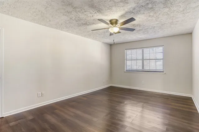 an empty room with wooden floor fan and windows