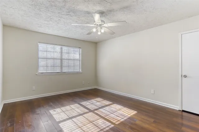 an empty room with wooden floor chandelier fan and windows