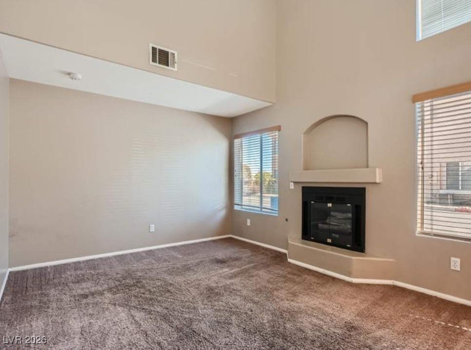 3950 South Sandhill Road, Unit 121 Las Vegas, NV 89121 - Photo 10 of 11 Unfurnished living room with carpet, a glass covered fireplace, and a high ceiling
