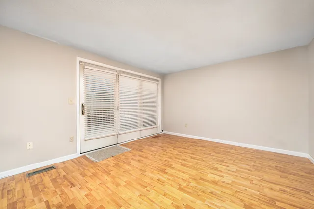 a view of an empty room with wooden floor and a window