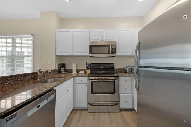 a kitchen with stainless steel appliances granite countertop a stove top oven a sink dishwasher a microwave oven and a dining table with wooden floor