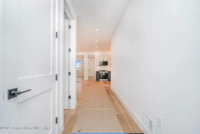 a view of a hallway with wooden floor and a bathroom