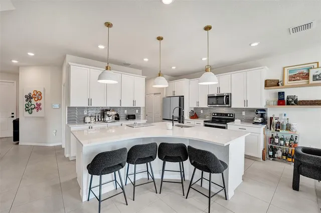 a kitchen with stainless steel appliances a stove a sink a kitchen island with chairs and white cabinets