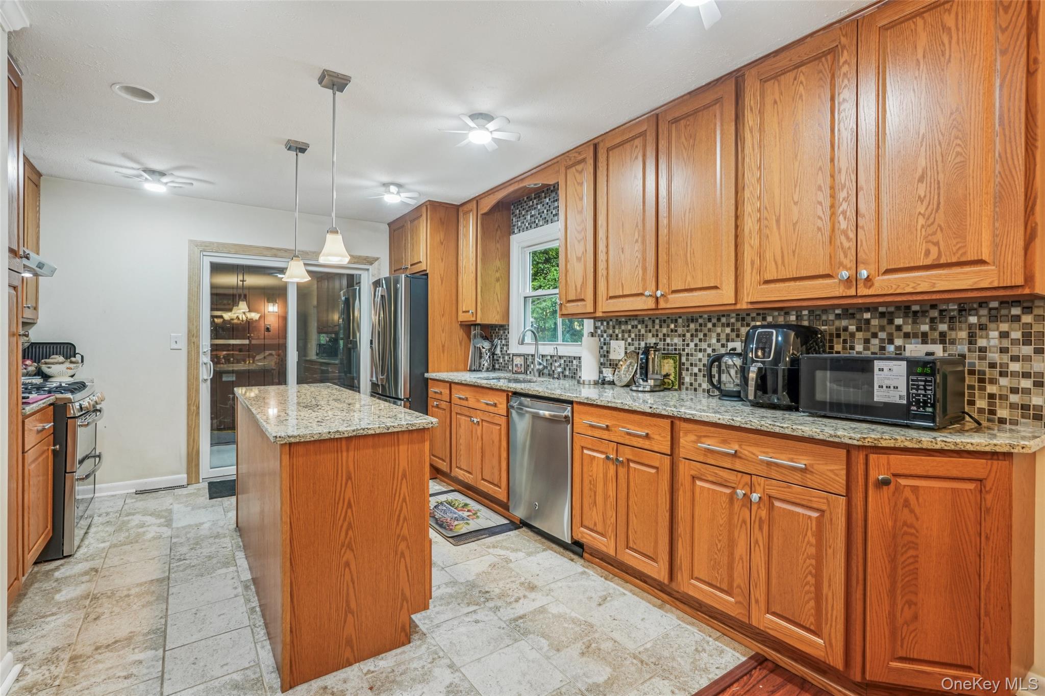 11 Hustis Road Cold Spring, NY 10516 - Photo 8 of 31 Kitchen with brown cabinetry, light stone counters, backsplash, a kitchen island, and decorative light fixtures