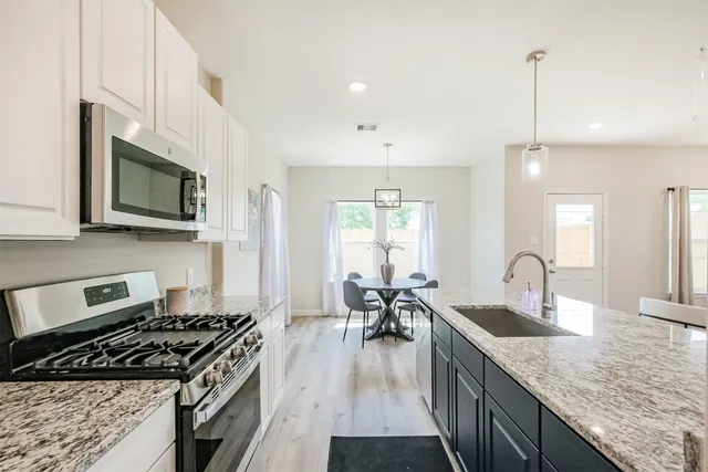 a kitchen with granite countertop a stove a sink a dining table and chairs