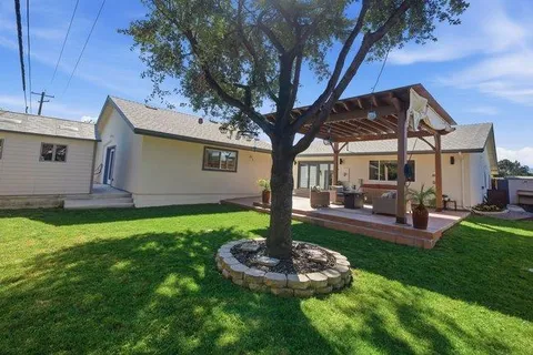 a view of a backyard with table and chairs potted plants and large tree