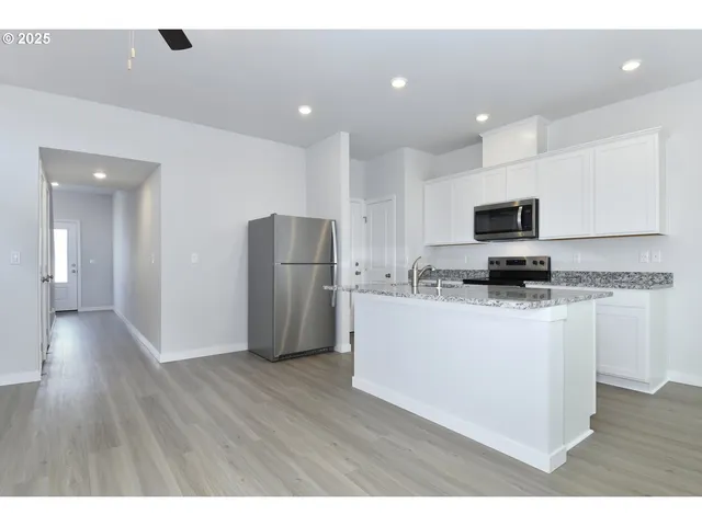 a kitchen with stainless steel appliances granite countertop a refrigerator a stove top oven a sink and a granite counter tops with wooden floors