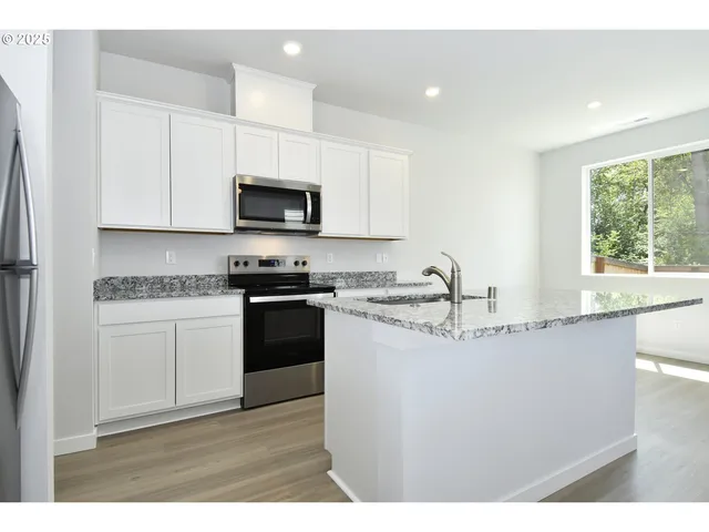 a kitchen with granite countertop a sink a stove a microwave a counter top space and cabinets