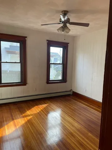 an empty room with wooden floor chandelier fan and windows