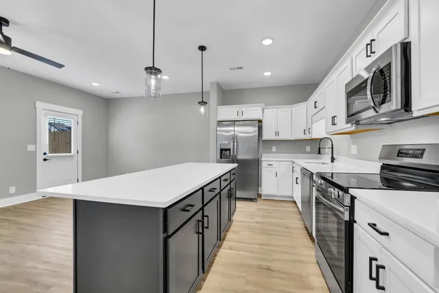 a kitchen with stainless steel appliances granite countertop a white stove top oven a sink dishwasher and a refrigerator with wooden floor