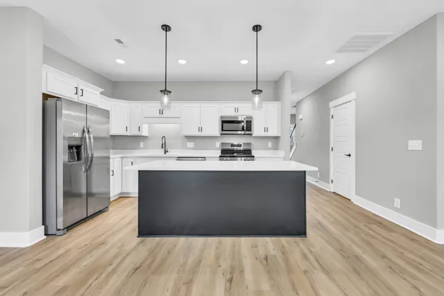 a kitchen with stainless steel appliances granite countertop a refrigerator a oven a sink and white cabinets with wooden floor