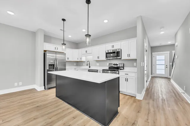 a kitchen with stainless steel appliances kitchen island granite countertop a refrigerator a sink dishwasher a stove and white cabinets with wooden floor