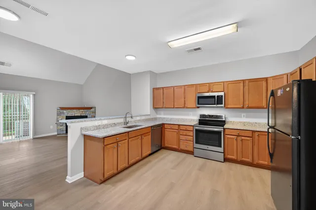 a kitchen with stainless steel appliances granite countertop a stove top oven a refrigerator a sink and dishwasher with wooden floor