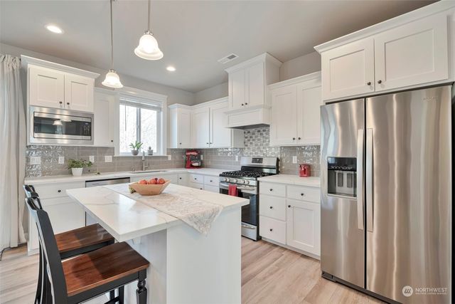 a kitchen with stainless steel appliances a refrigerator a stove a sink dishwasher a stove and white cabinets with wooden floor