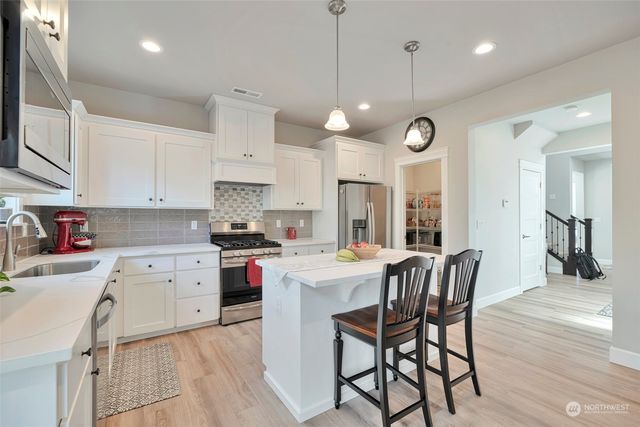 a kitchen with kitchen island granite countertop a sink a stove a refrigerator and white cabinets with wooden floor