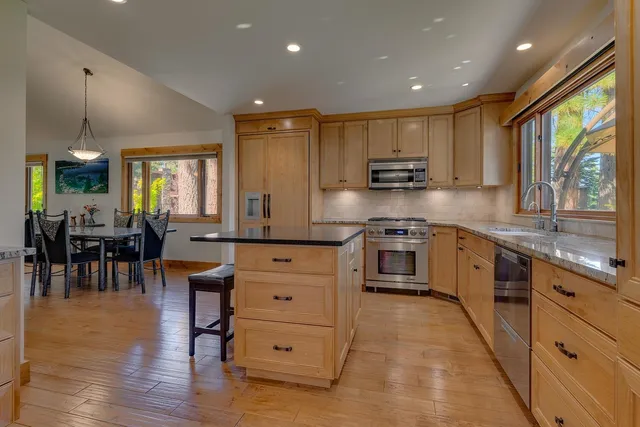 a kitchen with stainless steel appliances granite countertop a stove top oven a sink dishwasher a dining table and chairs with wooden floor