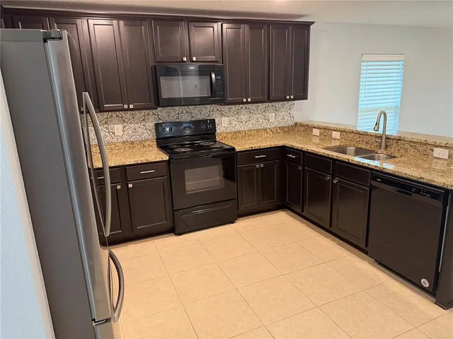 a kitchen with stainless steel appliances granite countertop a refrigerator a sink a stove a microwave and wooden cabinets