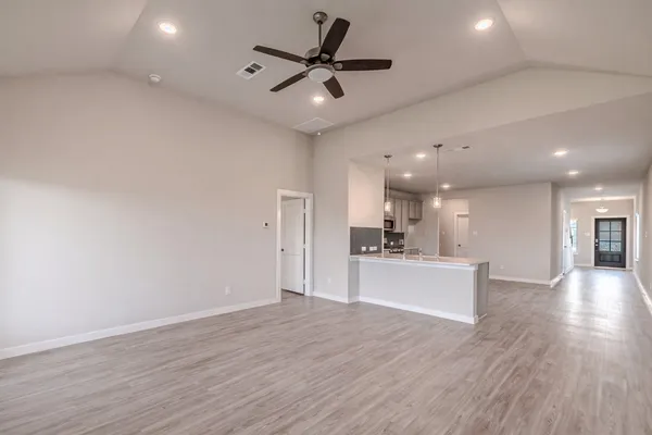 a view of an empty room and kitchen with wooden floor