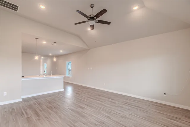 an empty room with wooden floor fan and windows