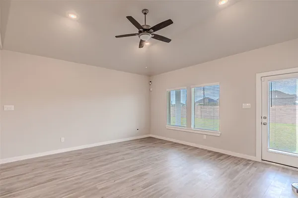 an empty room with wooden floor fan and windows