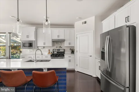 a kitchen with stainless steel appliances granite countertop a refrigerator a sink dishwasher a stove a dining table and chairs with wooden floor