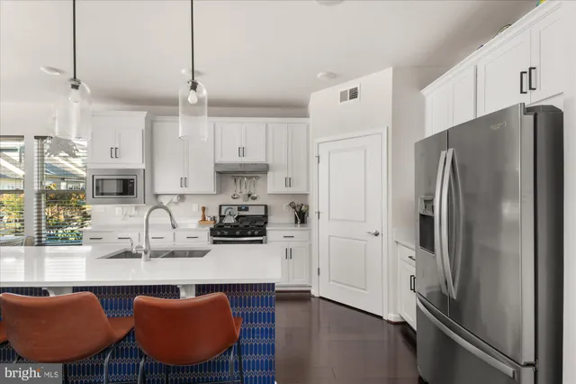 a kitchen with stainless steel appliances granite countertop a refrigerator a sink dishwasher a stove a dining table and chairs with wooden floor