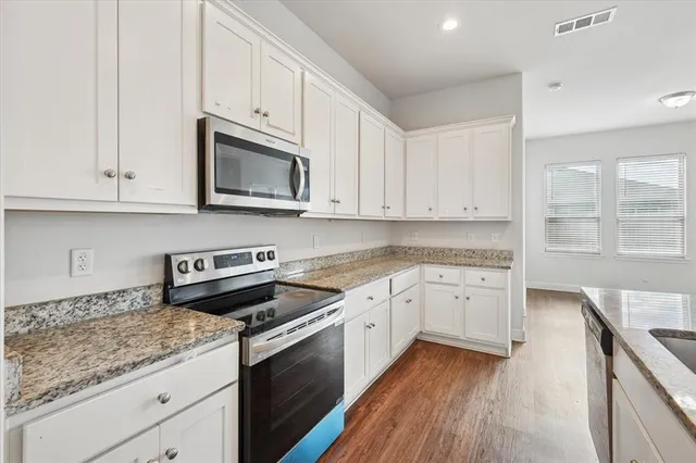 a kitchen with stainless steel appliances granite countertop a refrigerator a sink dishwasher a stove and white cabinets with wooden floor