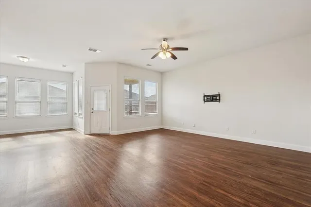an empty room with wooden floor chandelier fan and windows