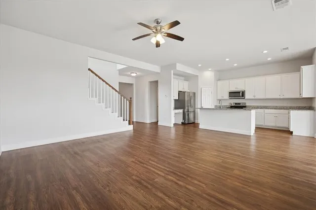 a view of an empty room with wooden floor and a kitchen