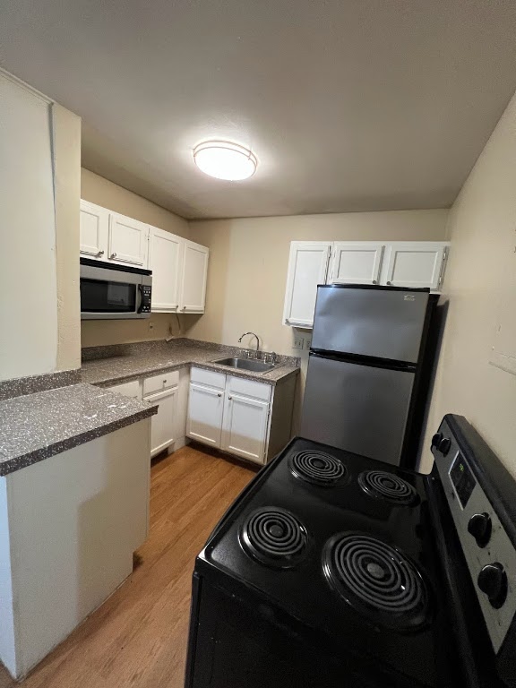 1000 West 26th Street, Unit 101 Austin, TX 78705 - Photo 5 of 10 Kitchen with white cabinets, light wood-style floors, appliances with stainless steel finishes, and a sink