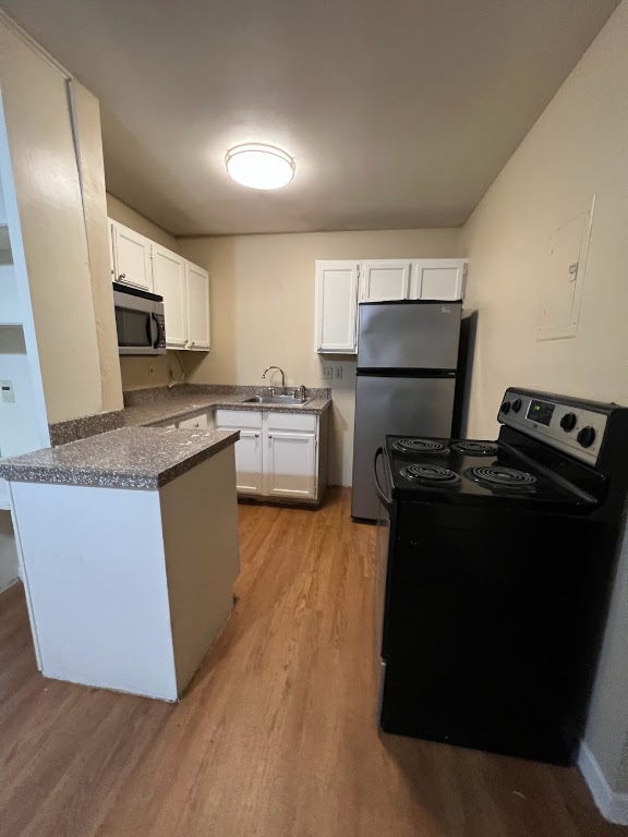 1000 West 26th Street, Unit 101 Austin, TX 78705 - Photo 7 of 10 Kitchen featuring white cabinets, a sink, light wood-type flooring, a peninsula, and appliances with stainless steel finishes
