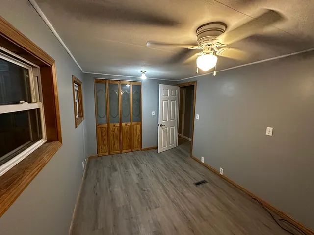 a view of an empty room with wooden floor and a ceiling fan