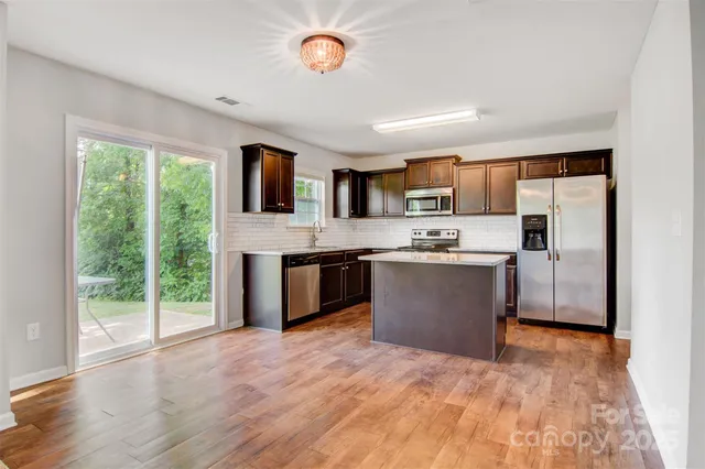 a large kitchen with stainless steel appliances granite countertop a stove top oven a sink dishwasher a refrigerator white cabinets and wooden floor