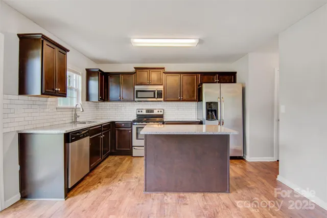 a kitchen with stainless steel appliances granite countertop a stove top oven a sink dishwasher and a refrigerator with wooden floor