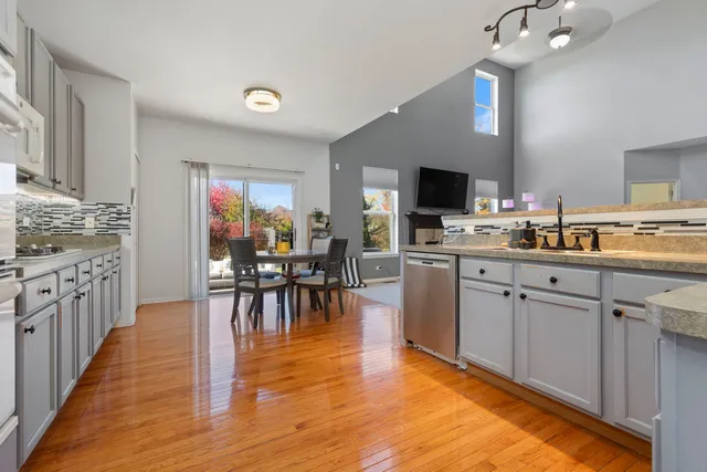 a kitchen with stainless steel appliances granite countertop a stove top oven a sink dishwasher and white cabinets with wooden floor