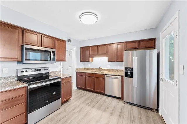 a kitchen with stainless steel appliances granite countertop a refrigerator a stove top oven a sink and dishwasher with wooden floor