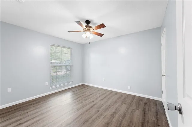 an empty room with wooden floor fan and windows