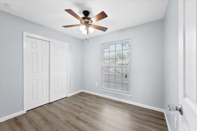 an empty room with wooden floor chandelier fan and windows