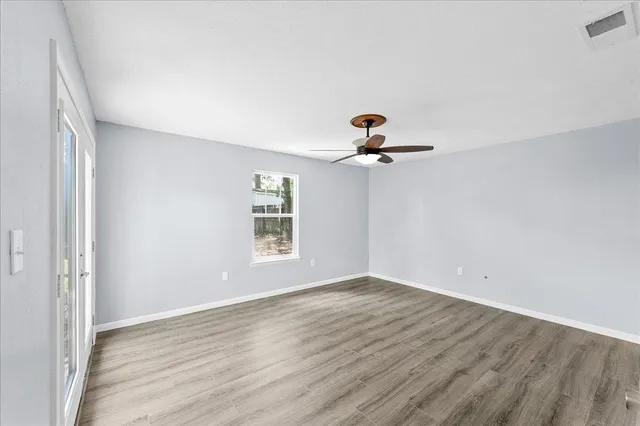 an empty room with wooden floor chandelier fan and windows