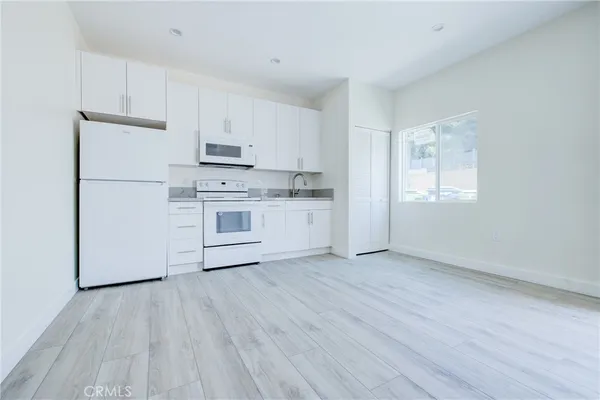 a kitchen with stainless steel appliances granite countertop a stove top oven a sink and white cabinets with wooden floor