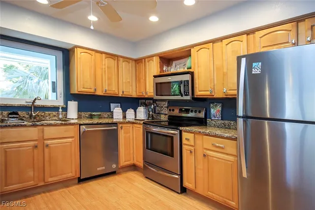 a kitchen with stainless steel appliances granite countertop a refrigerator a microwave oven a sink dishwasher and white cabinets with wooden floor