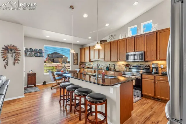 a kitchen with stainless steel appliances kitchen island granite countertop a stove top oven a sink a dining table and chairs with wooden floor