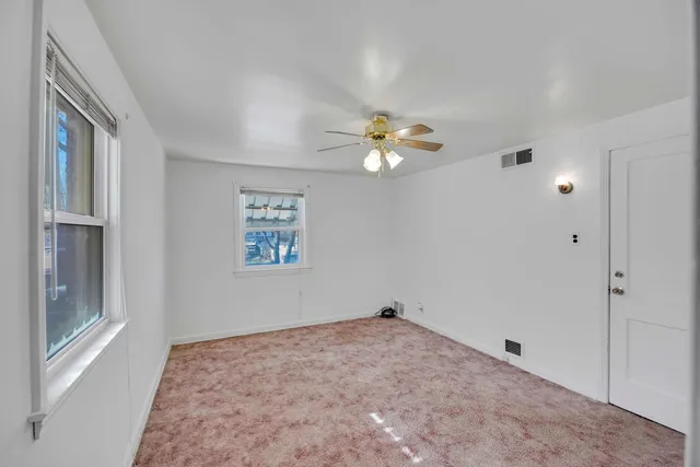 an empty room with a chandelier fan and windows