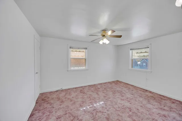 an empty room with a chandelier fan and windows